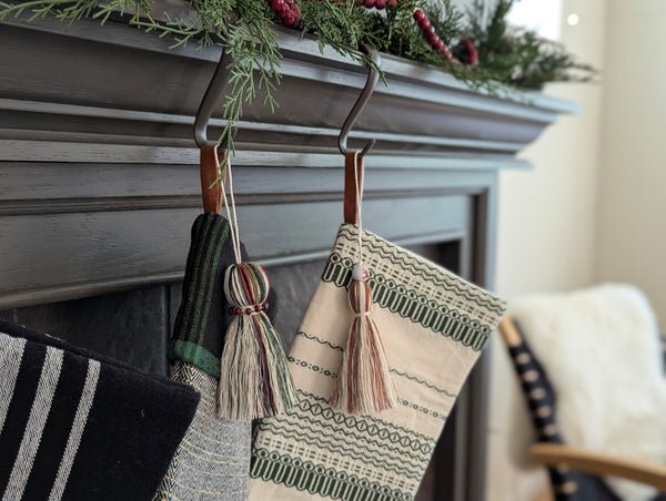 Decorative stockings with tassel tags hanging above a fireplace.