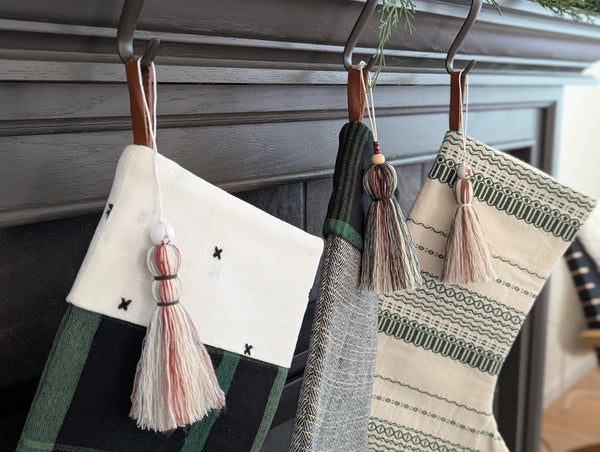 three Christmas stockings with tassel ornaments hanging on a fireplace mantle