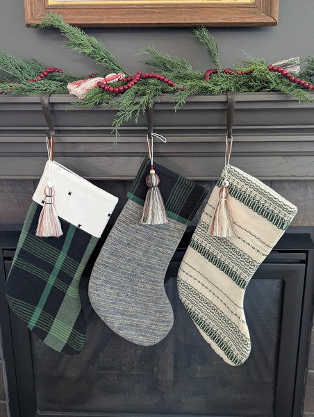 Three Christmas stockings hanging on a fireplace mantle with cotton holiday tassels and garlands