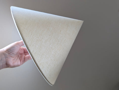 hand holding a cone lamp shade near a window with light shining through the lamp shade