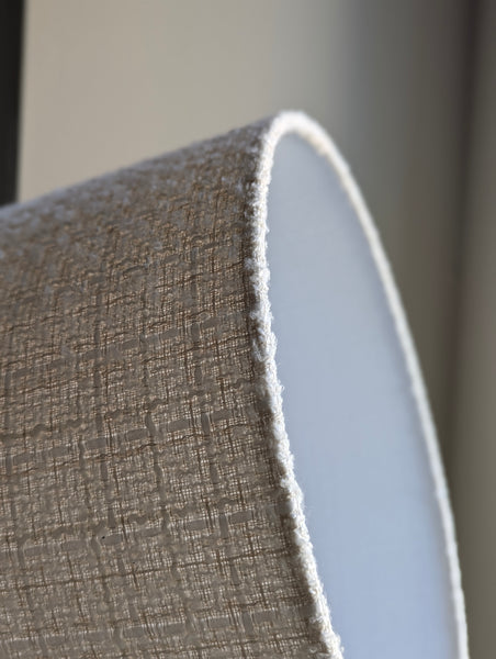 close up of a tweed boucle lamp shade in front of a window with sunlight shining through it