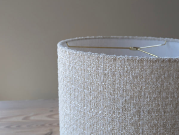 Close-up of a textured boucle lamp shade with brass hardware on a light wood table