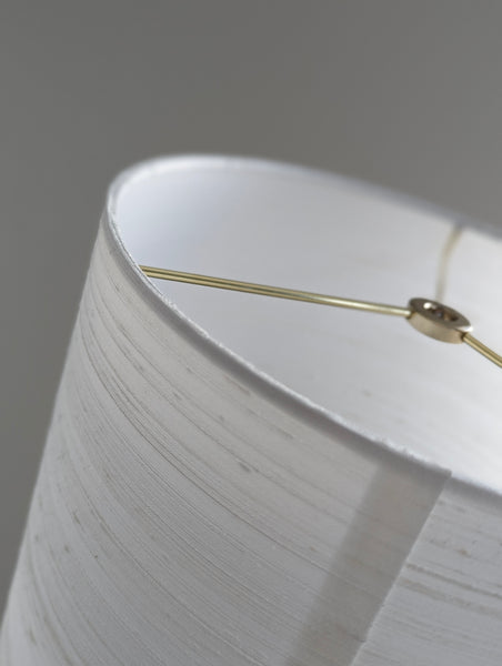 Close-up of a white textured fabric lampshade with brass spider washer hardware