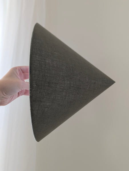 hand holding a cone shaped lamp shade in green linen fabric