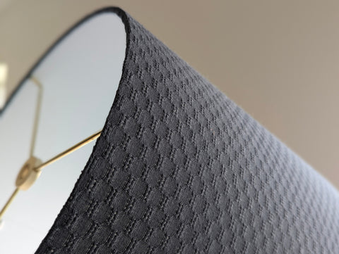 a close up showing the lamp shade at an angle that shows the woven texture of the gray jacquard fabric