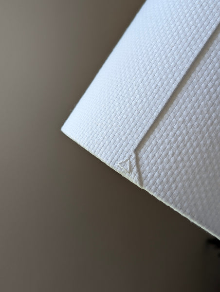Close-up of a white textured lampshade in Bright White Crosshatch fabric against a soft gray background