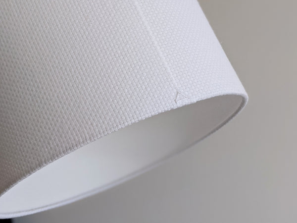 Close-up of a white textured lampshade in Bright White Crosshatch fabric against a soft gray background