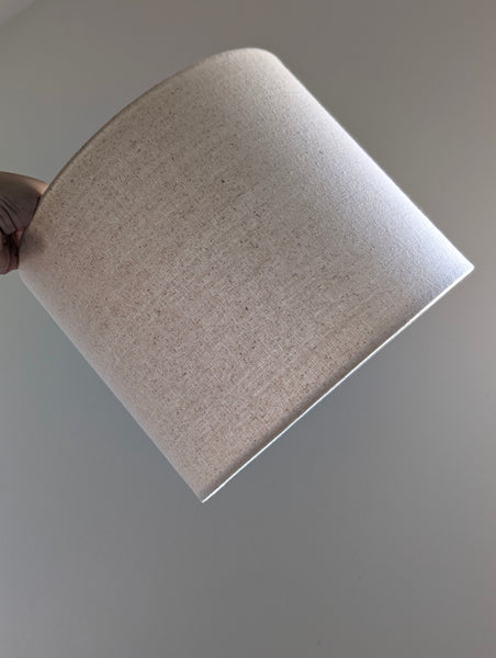 Speckled Oatmeal cotton fabric lampshade with brass hardware against a blurred background