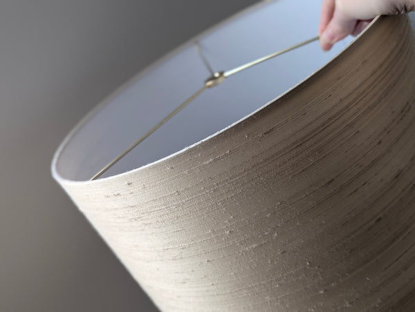 Close-up of a drum lampshade in silk with a hand holding the fixture against a neutral background