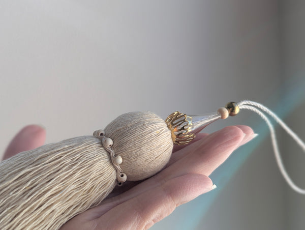 Decorative tassel held in a hand against a neutral background
