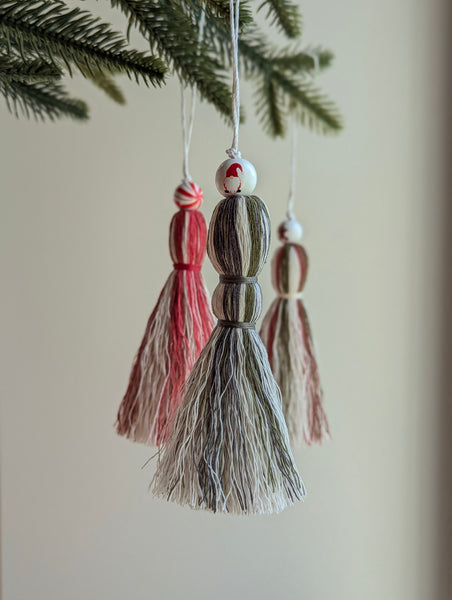 Tassel gnome ornament hanging from a branch with two other tassels