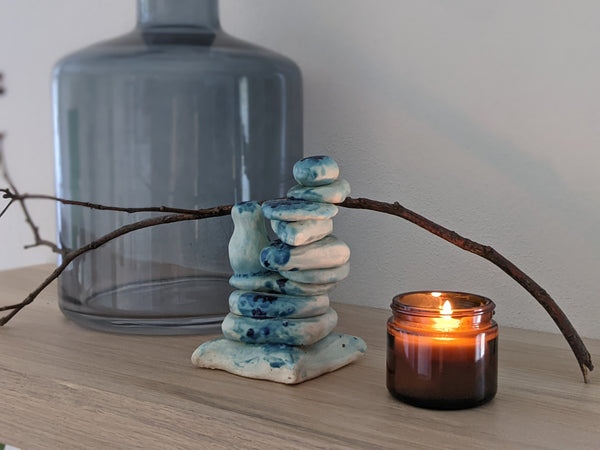 an amber glass candle with the label removed on an oak shelf with a ceramic sculpture