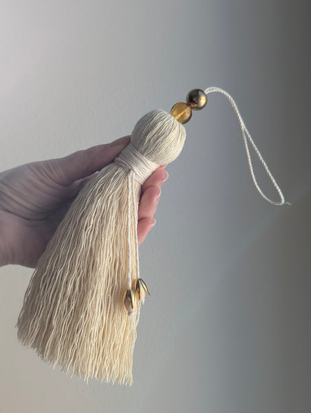 Hand holding a beige tassel with a brass bead against a gray background