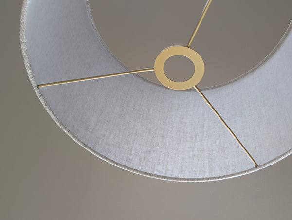 Speckled Oatmeal cotton fabric lampshade with brass hardware against a blurred background