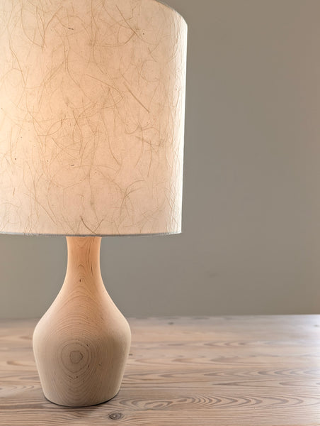 wooden table lamp with a textured beige paper shade on a wooden table