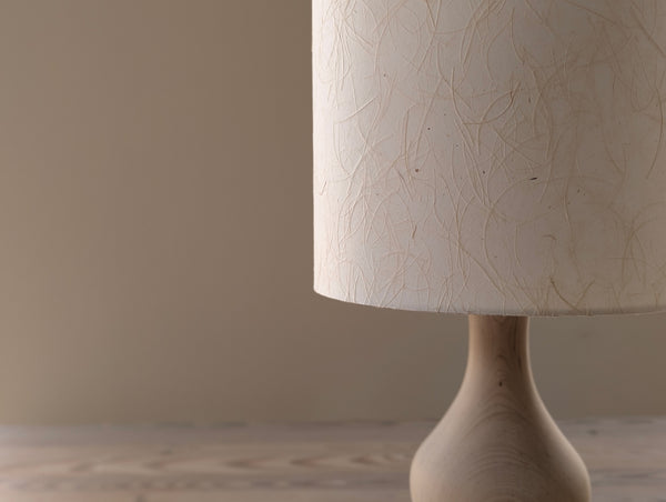 Close-up of a beige textured lampshade on a wooden base against a neutral background