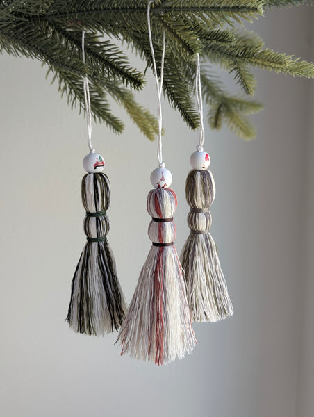 Three tassel ornaments hanging from a Christmas tree branch against a neutral background