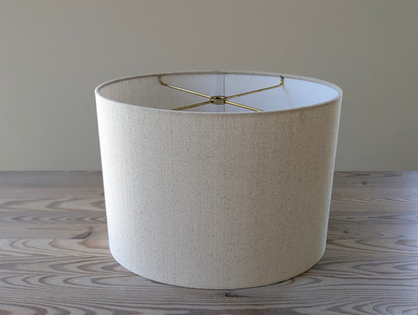 oval lampshade in a natural fabric and brass hardware sitting on a wooden table
