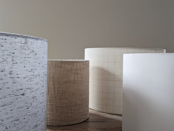 four lamp shades in different fabrics sit on a light wood table