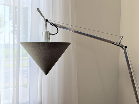 Modern wall-mounted lamp with an olive green cone-shaped shade against a neutral wall in front of a window
