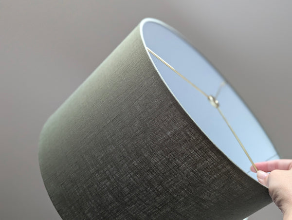 Close-up of an olive green lampshade with a linen textured fabric exterior and a white inner lining against a neutral background