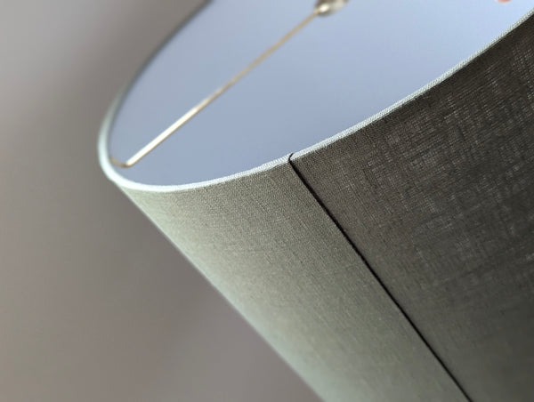 Close-up of an olive green lampshade with a linen textured fabric exterior and a white inner lining against a neutral background