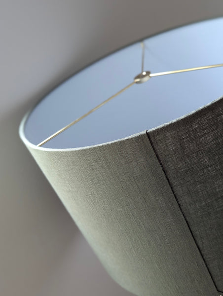 Close-up of an olive green lampshade with a linen textured fabric exterior and a white inner lining against a neutral background