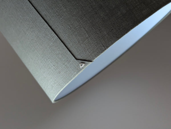 Close-up of an olive green lampshade with a linen textured fabric exterior and a white inner lining against a neutral background