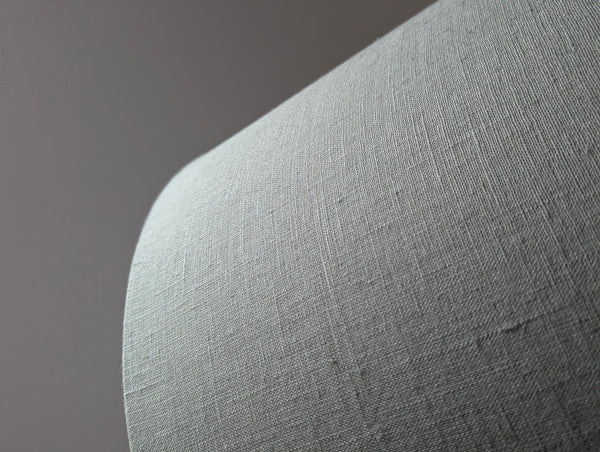 Close-up of an olive green lampshade with a linen textured fabric exterior and a white inner lining against a neutral background