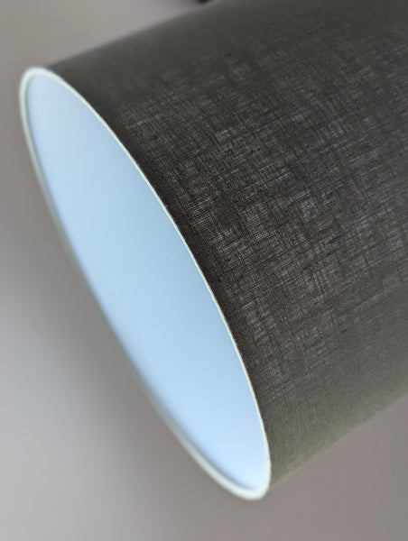 Close-up of an olive green lampshade with a linen textured fabric exterior and a white inner lining against a neutral background