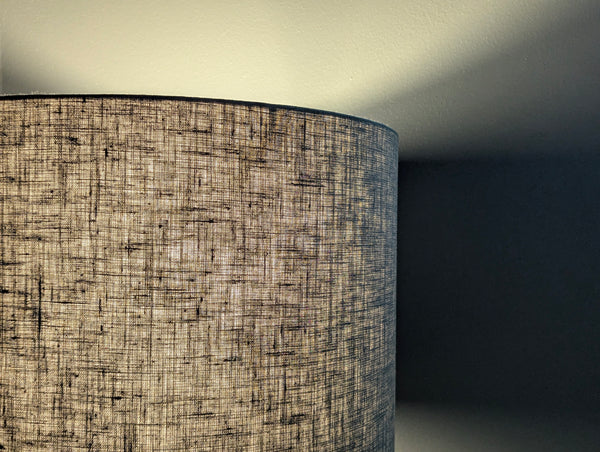 Close-up of an olive green lampshade with a linen textured fabric exterior and a white inner lining against a neutral background