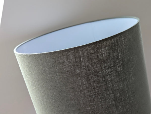 Close-up of an olive green lampshade with a linen textured fabric exterior and a white inner lining against a neutral background