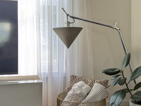 Modern arching lamp with an olive green cone-shaped shade in a living room with a TV stand, blanket basket and plant