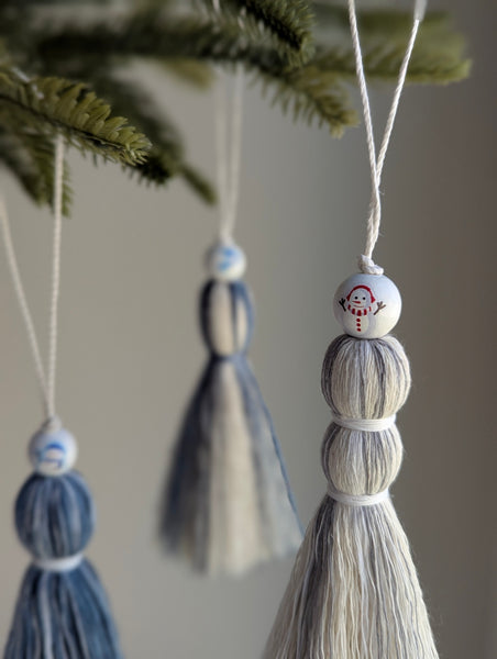 Holiday tassel ornaments with snowman beads hanging from a Christmas tree 
