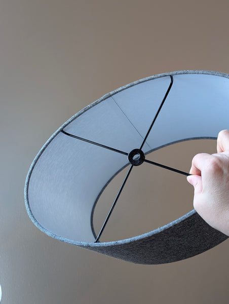 Gray lampshade held by a hand against a neutral background