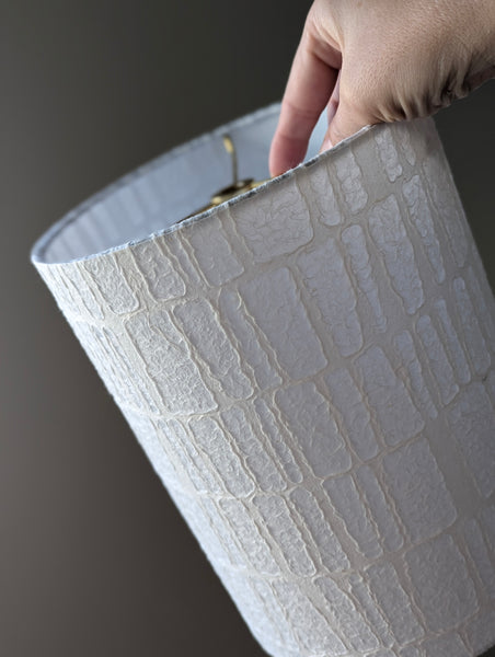 Hand holding a textured white lampshade against a dark background