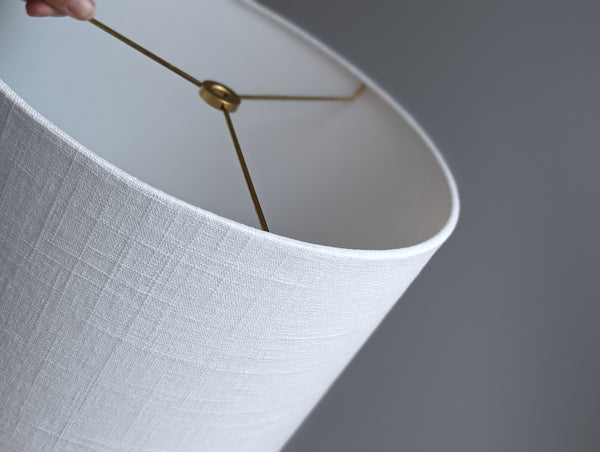 Close-up of a white linen lamp shade with brass spider washer hardware against a neutral background