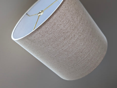 Speckled Oatmeal cotton fabric lampshade with brass hardware against a blurred background