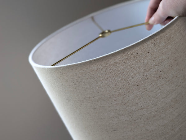 Speckled Oatmeal cotton fabric lampshade with brass hardware against a blurred background