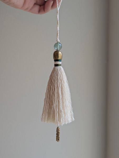 a small festive door tassel made of cotton with a green glass bead and brass accents