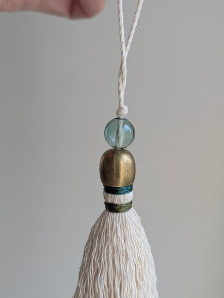 a small festive door tassel made of cotton with a green glass bead and brass accents