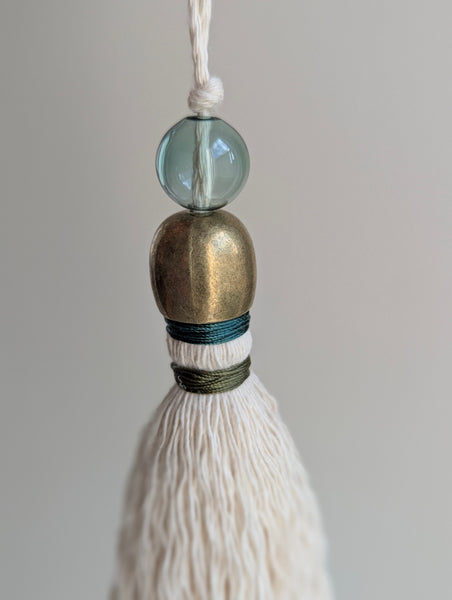 a small festive door tassel made of cotton with a green glass bead and brass accents