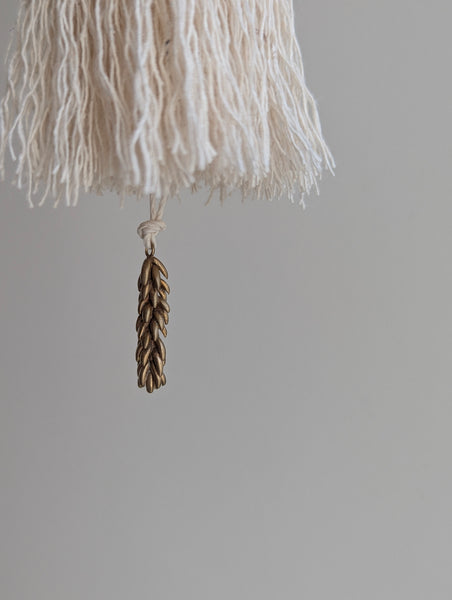 a small festive door tassel made of cotton with a green glass bead and brass accents
