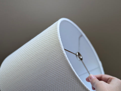 Close-up of a white textured lampshade with a visible woven pattern with nickel hardware