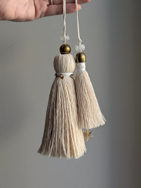 snowy white snowflake tassel with white speckled glass bead and brass snowflake charm hanging next to a larger tassel with white and brass accents