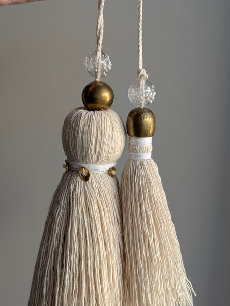 snowy white snowflake tassel with white speckled glass bead and brass snowflake charm hanging next to a larger tassel with white and brass accents