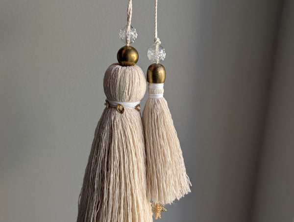 snowy white snowflake tassel with white speckled glass bead and brass snowflake charm hanging next to a larger tassel with white and brass accents