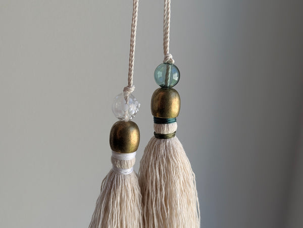 snowy white snowflake tassel with white speckled glass bead and brass snowflake charm hanging next to a green version of the same tassel