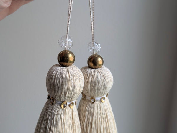 two snowy white tassels in a natural cotton color with brass accents and a handblown glass bead