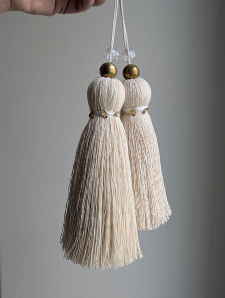 two snowy white tassels in a natural cotton color with brass accents and a handblown glass bead
